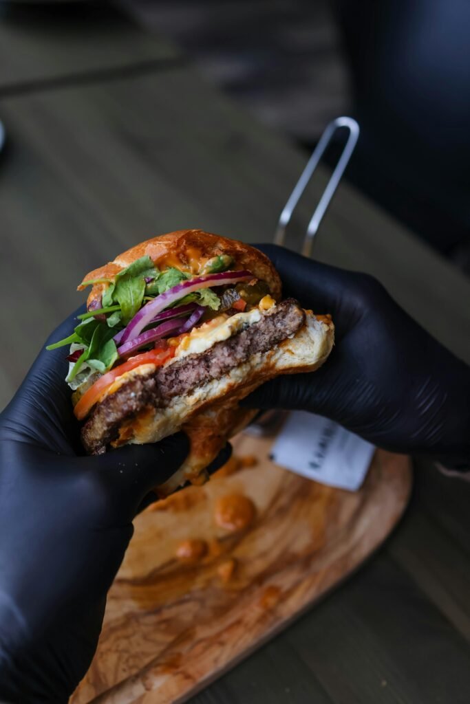 Close-up of a delicious beef burger with fresh veggies held by hands.